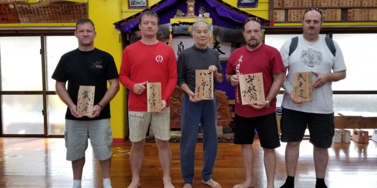 History tour participants holding wooden plaques in a dojo