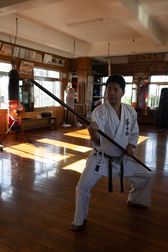 Karateka performing a bo staff kata in a sunlit dojo