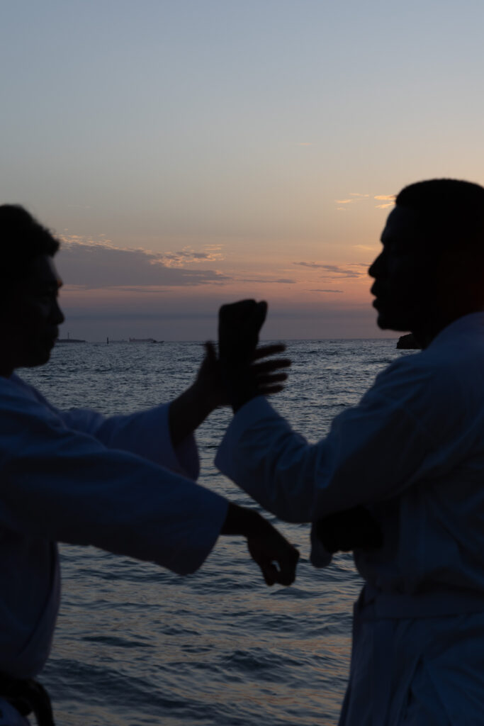 Two karateka silhouetted against an Okinawan sunset