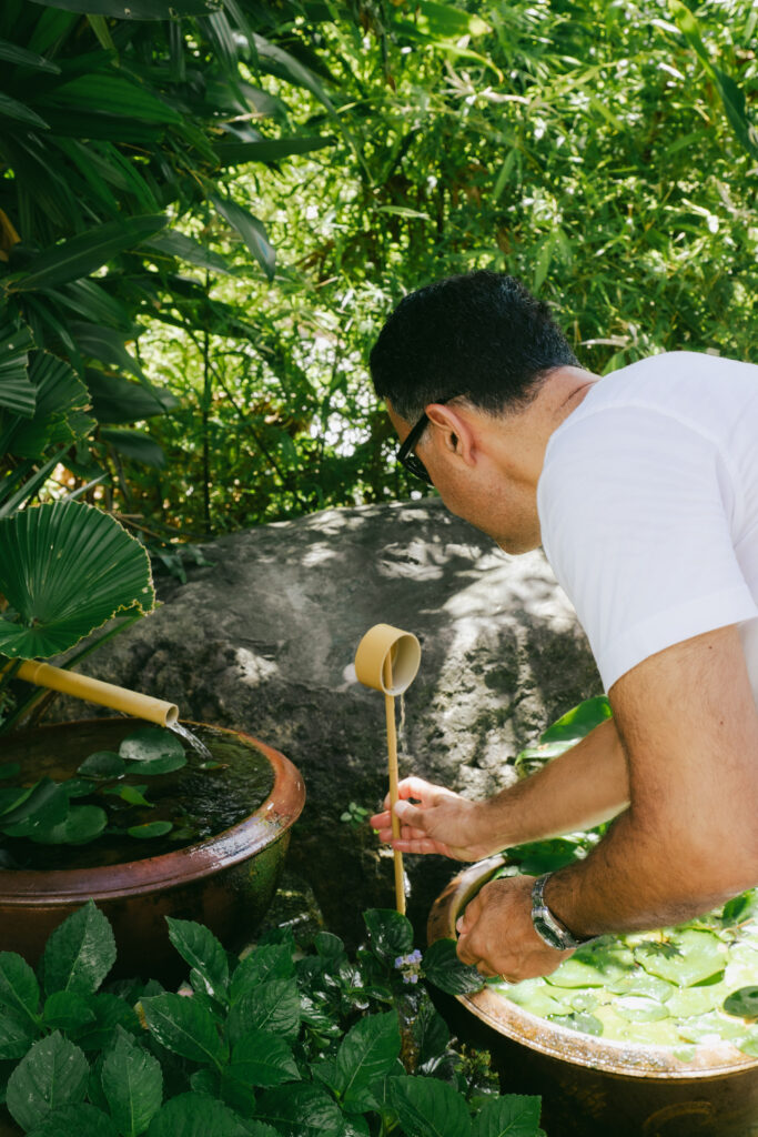 Visitor scooping water at a stone basin in a tropical garden
