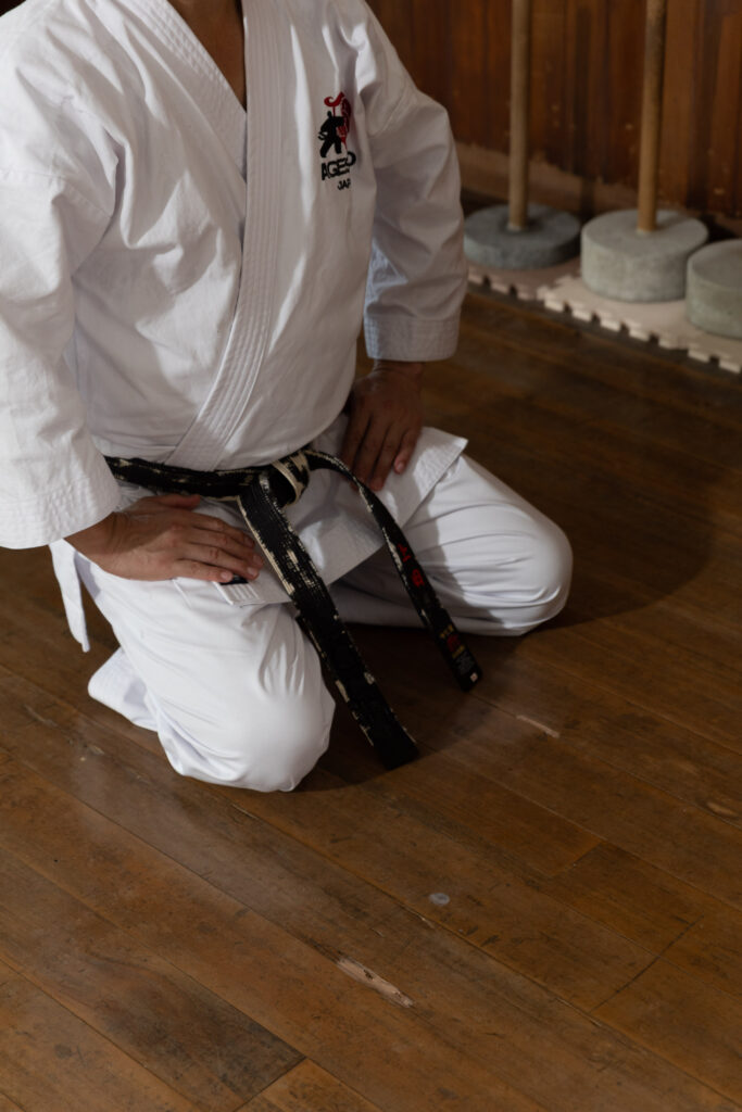 Karateka kneeling and tying his black belt on a wooden floor