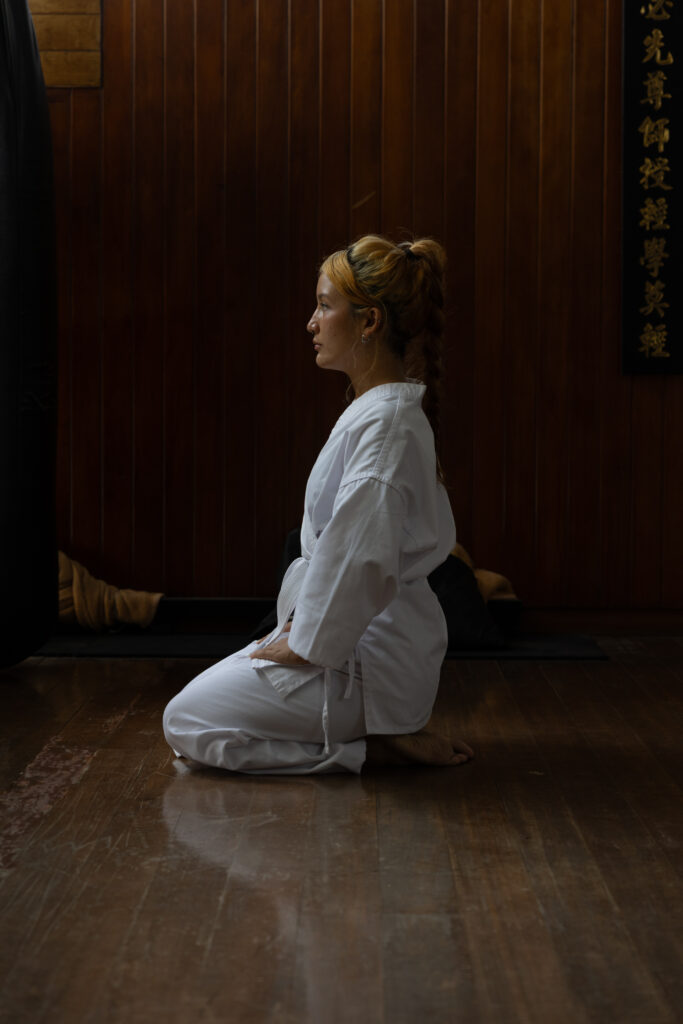 Karate student kneeling in seiza in a dark wooden dojo