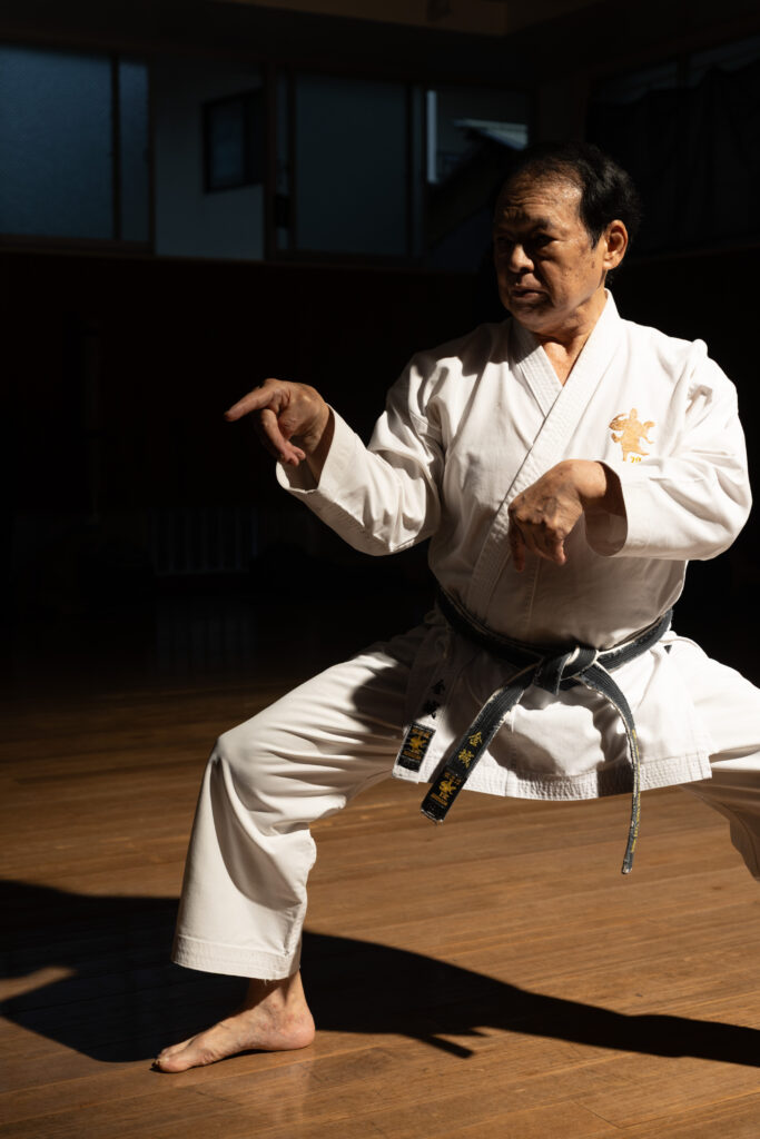 Okinawan karate master in a low stance in a sunlit dojo