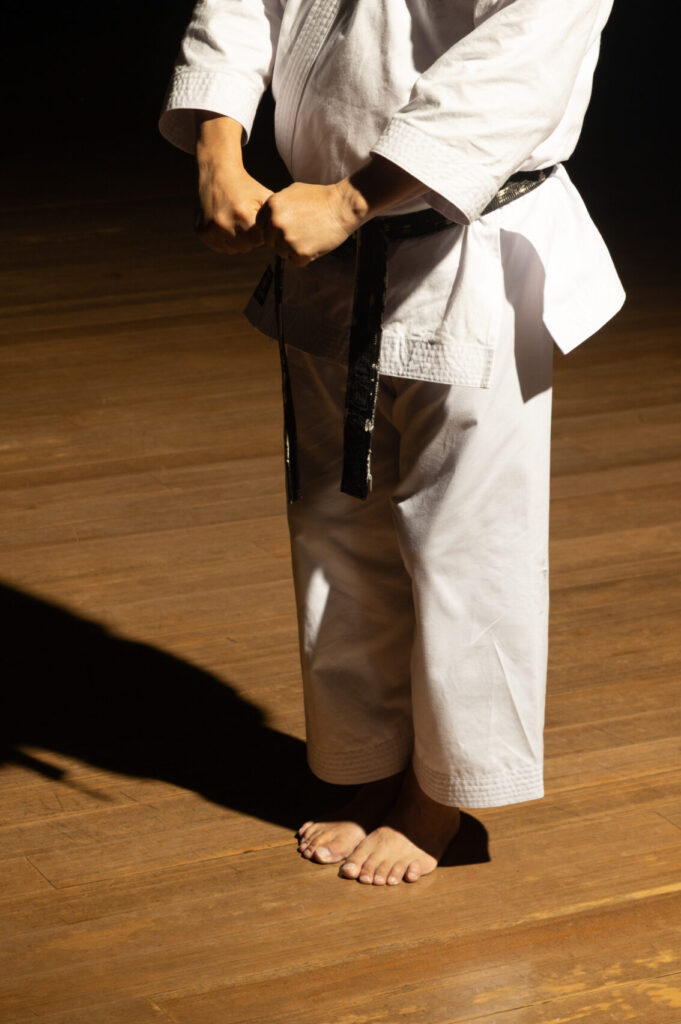 Karateka in a white gi and black belt standing on a wooden dojo floor