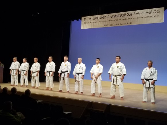 Karate and kobudo masters on stage at a charity demonstration