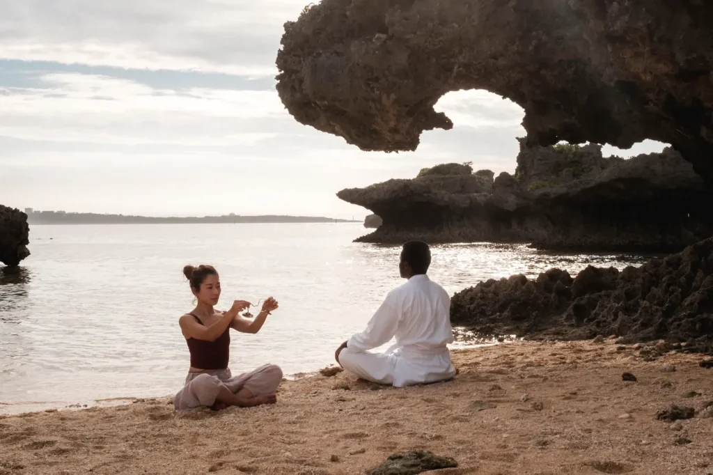 Two people seated in meditation on a beach at sunset